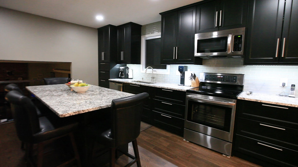 Bild på ett mellanstort funkis flerfärgad flerfärgat kök och matrum, med en undermonterad diskho, skåp i shakerstil, svarta skåp, granitbänkskiva, grått stänkskydd, stänkskydd i glaskakel, rostfria vitvaror, mellanmörkt trägolv, en köksö och brunt golv