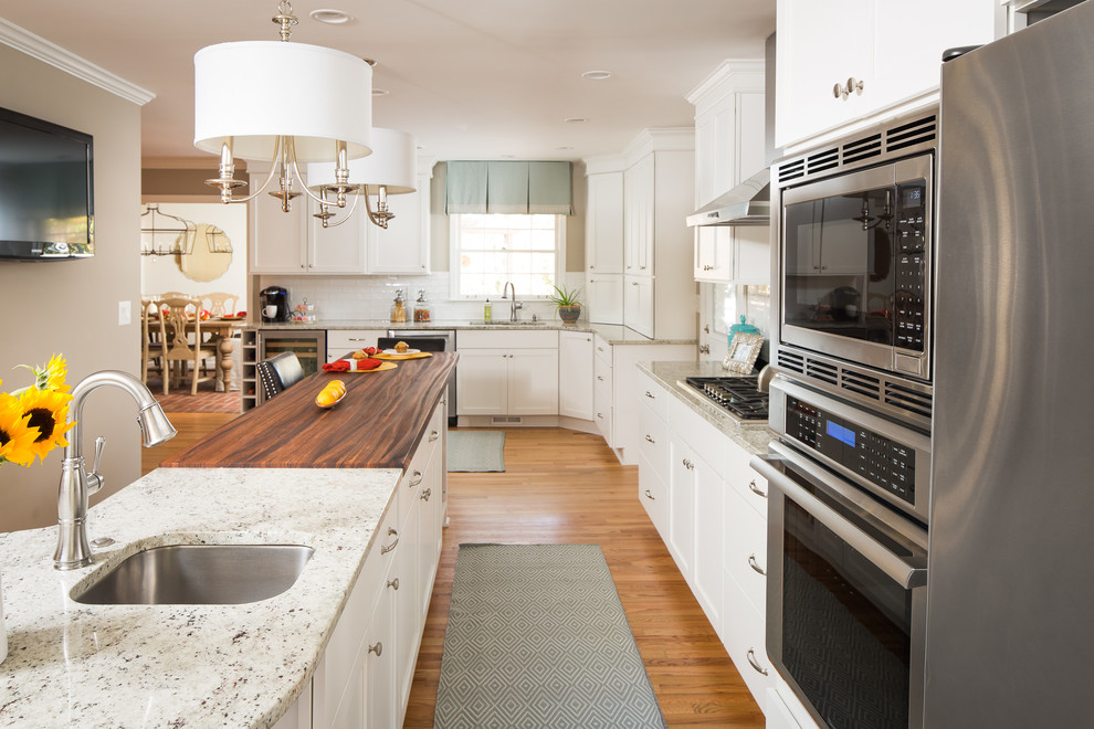 Medium sized classic l-shaped kitchen/diner in Atlanta with a submerged sink, shaker cabinets, white cabinets, white splashback, an island, brown floors, engineered stone countertops, ceramic splashback, stainless steel appliances, light hardwood flooring and white worktops.