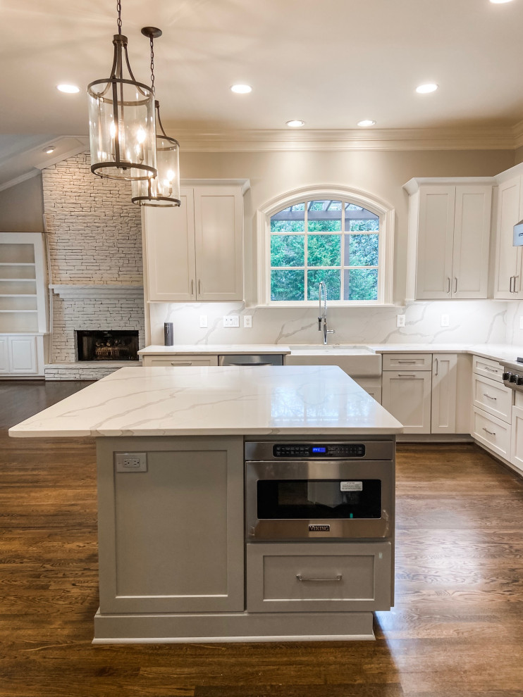 Photo of a large traditional l-shaped open plan kitchen in Atlanta with a belfast sink, shaker cabinets, white cabinets, engineered stone countertops, white splashback, engineered quartz splashback, stainless steel appliances, dark hardwood flooring, an island, green floors and white worktops.