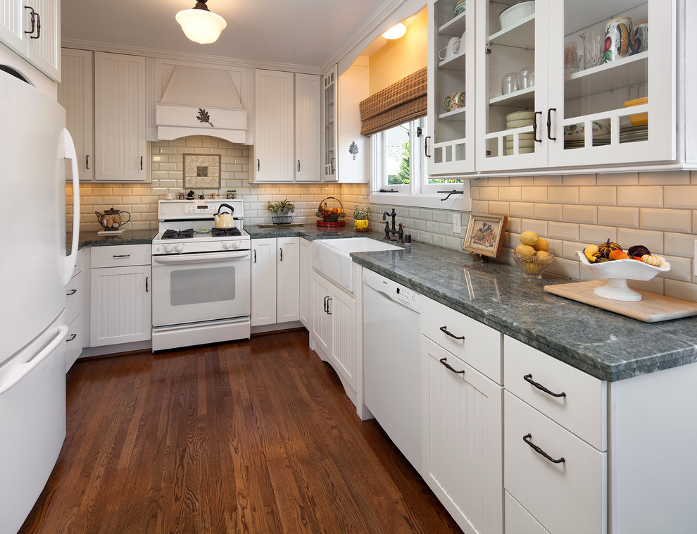 Example of an arts and crafts dark wood floor kitchen design in Santa Barbara with a farmhouse sink, beaded inset cabinets, white cabinets, marble countertops, beige backsplash, ceramic backsplash and white appliances