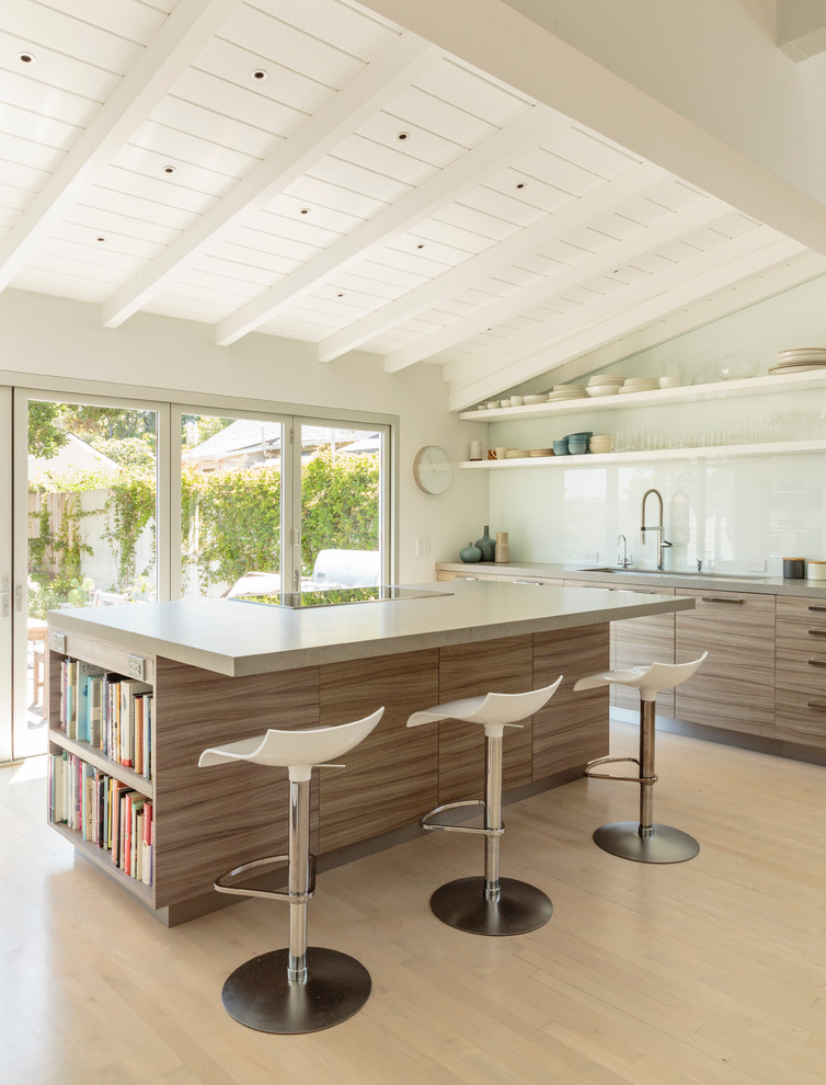 Moderne Küche mit flächenbündigen Schrankfronten, hellbraunen Holzschränken, Küchenrückwand in Weiß, Glasrückwand, hellem Holzboden und Kücheninsel in Santa Barbara