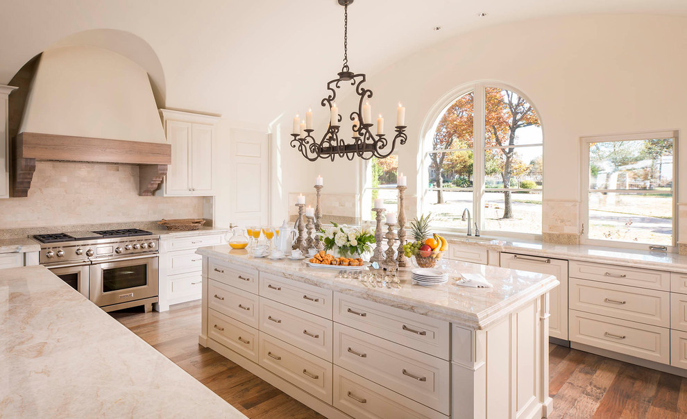 This is an example of a mediterranean kitchen in Dallas with a submerged sink, raised-panel cabinets, white cabinets, beige splashback, stainless steel appliances, medium hardwood flooring, an island and white worktops.