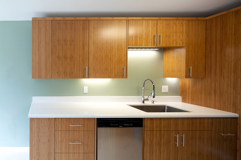 Idées déco pour une cuisine américaine parallèle moderne en bois brun avec un évier encastré, un placard à porte plane, un plan de travail en quartz modifié, une crédence blanche et un électroménager en acier inoxydable.