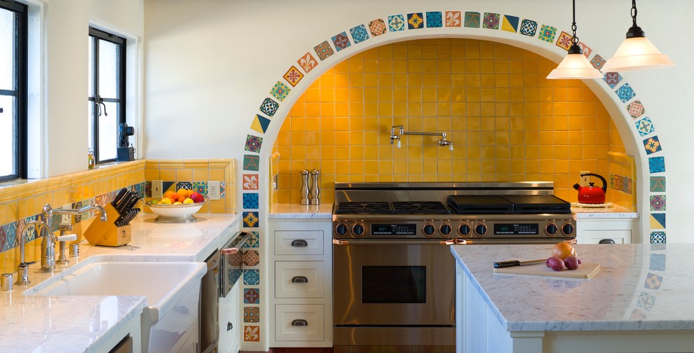 Ejemplo de cocina mediterránea con encimera de mármol, electrodomésticos de acero inoxidable, fregadero sobremueble, puertas de armario blancas y salpicadero amarillo