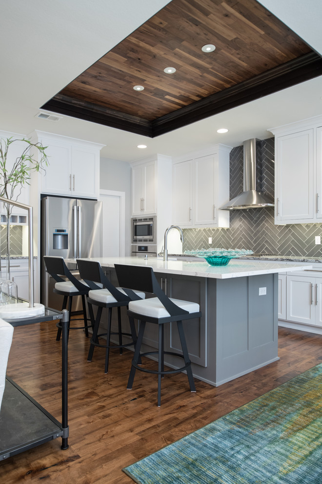 Modern inredning av ett kök och matrum, med en undermonterad diskho, vita skåp, bänkskiva i kvartsit, grått stänkskydd, stänkskydd i keramik, rostfria vitvaror, mörkt trägolv, en köksö och brunt golv