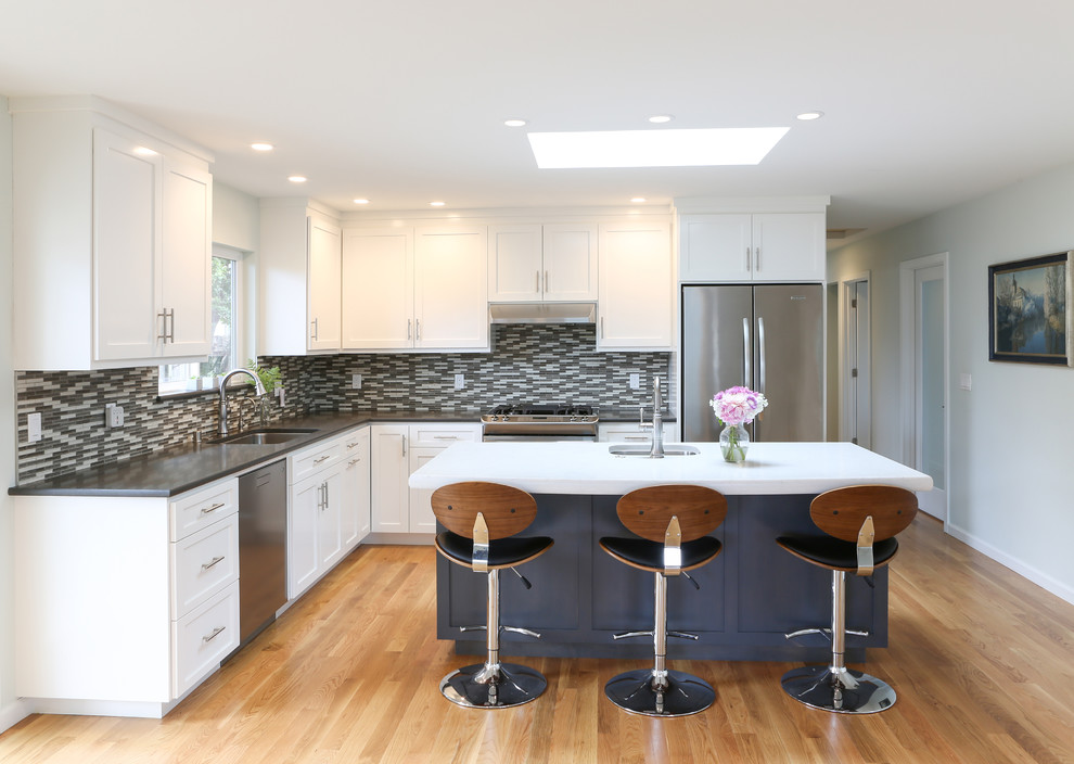 Inspiration for a large transitional l-shaped medium tone wood floor and brown floor kitchen remodel in San Francisco with an undermount sink, shaker cabinets, white cabinets, multicolored backsplash, glass tile backsplash, stainless steel appliances, an island and gray countertops