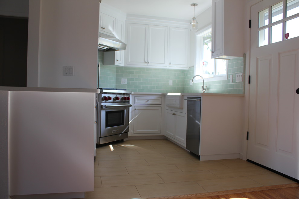 Maritim inredning av ett litet kök, med en rustik diskho, vita skåp, bänkskiva i kvarts, grönt stänkskydd, stänkskydd i glaskakel och rostfria vitvaror