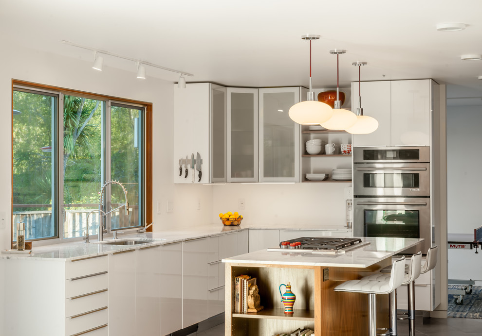 Bild på ett mellanstort 50 tals kök, med en enkel diskho, släta luckor, vita skåp, marmorbänkskiva, rostfria vitvaror, cementgolv, en köksö och grått golv