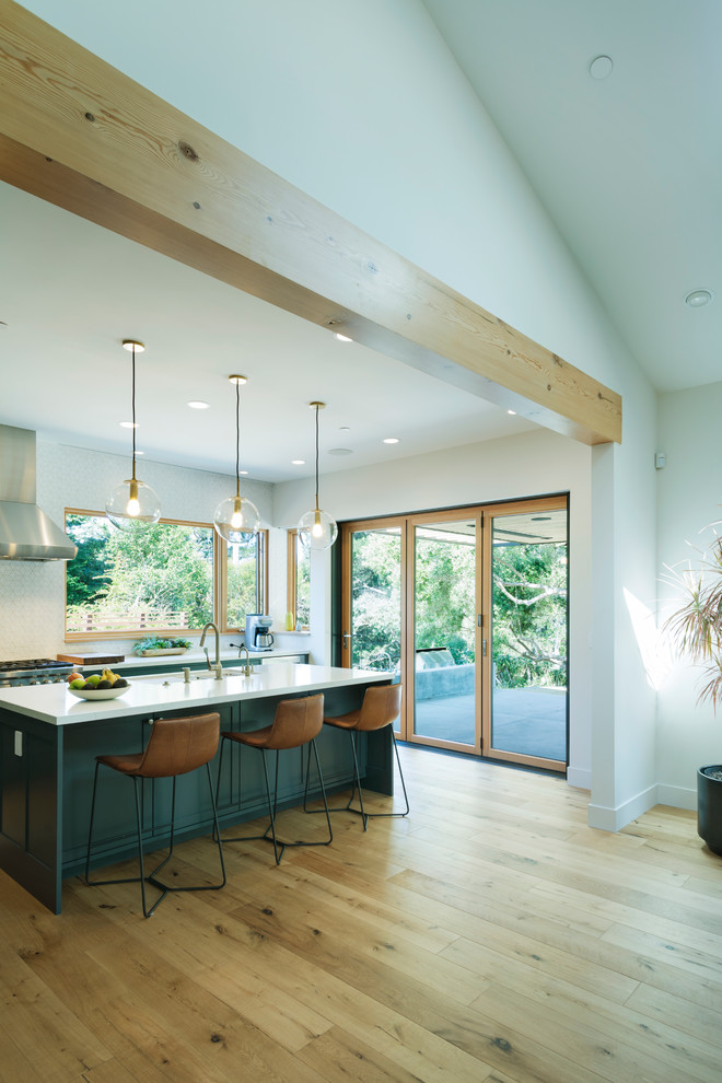 Inspiration for a large modern l-shaped light wood floor open concept kitchen remodel in San Francisco with a farmhouse sink, shaker cabinets, blue cabinets, quartz countertops, white backsplash, ceramic backsplash, stainless steel appliances, an island and white countertops