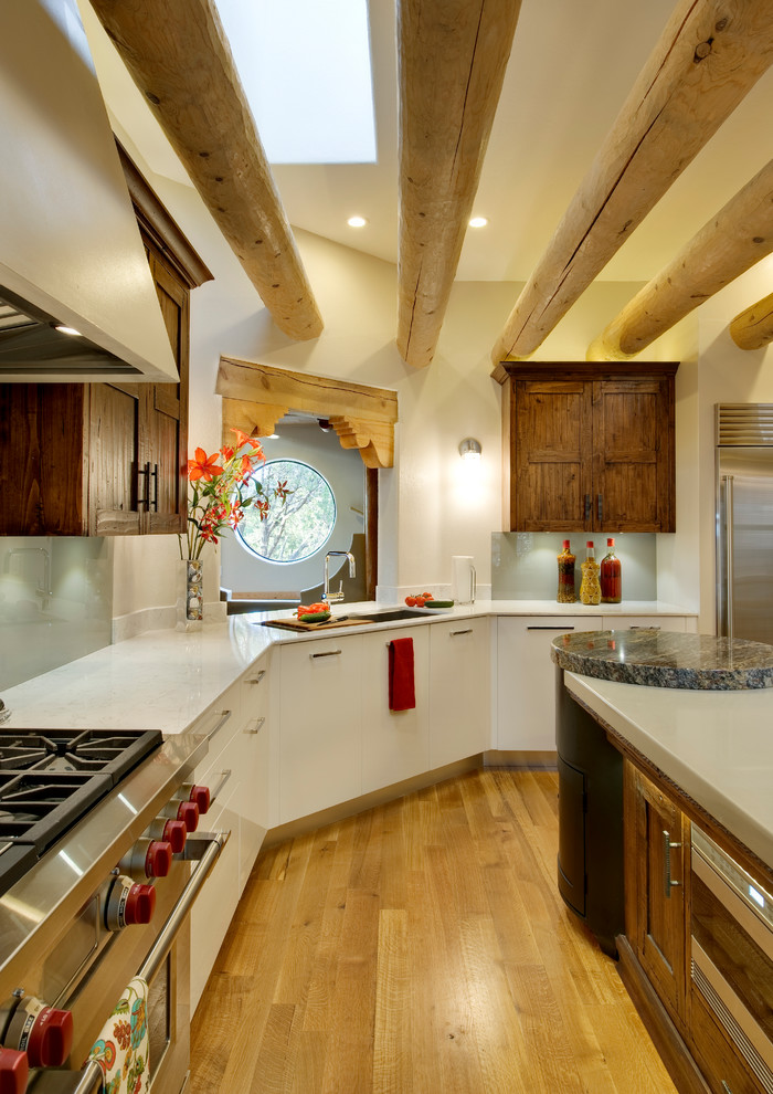 Large southwest l-shaped light wood floor enclosed kitchen photo in Albuquerque with flat-panel cabinets, white cabinets, glass sheet backsplash, an undermount sink, solid surface countertops and stainless steel appliances