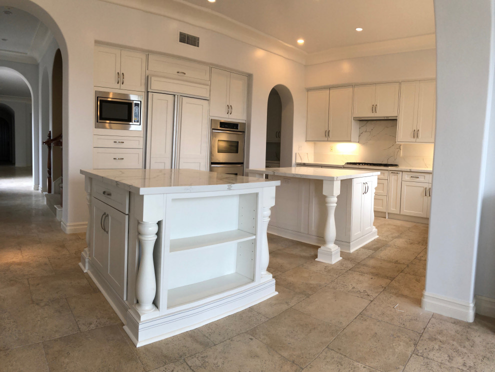 Example of a huge minimalist u-shaped travertine floor and beige floor kitchen design in San Diego with a single-bowl sink, shaker cabinets, white cabinets, quartzite countertops, white backsplash, quartz backsplash, stainless steel appliances, two islands and white countertops