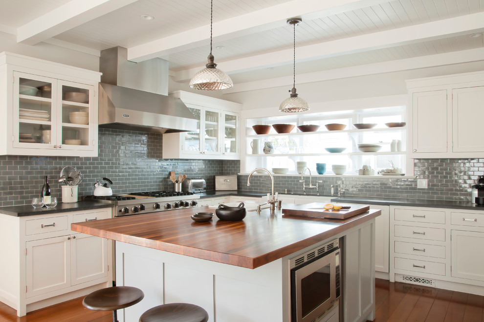 Kitchen - coastal kitchen idea in Los Angeles with glass-front cabinets, white cabinets, wood countertops, gray backsplash, subway tile backsplash and stainless steel appliances