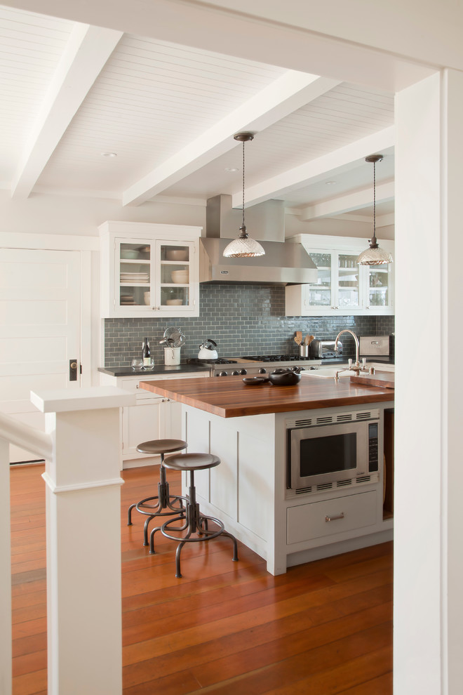 Inspiration for a coastal kitchen remodel in Los Angeles with glass-front cabinets, white cabinets, wood countertops, blue backsplash, subway tile backsplash and stainless steel appliances