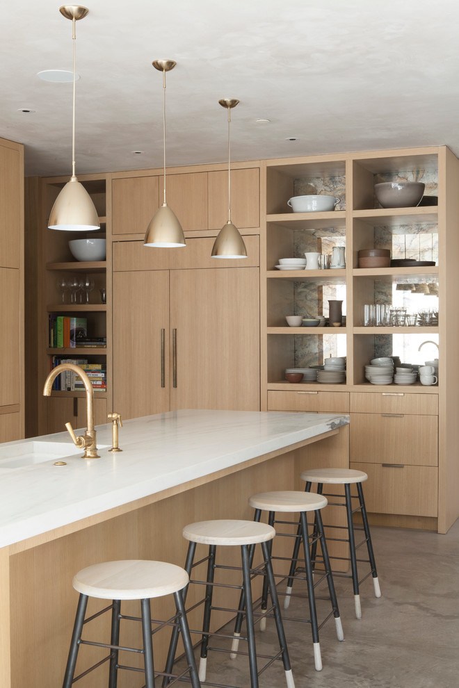 Свежая идея для дизайна: кухня-гостиная в стиле модернизм с плоскими фасадами, светлыми деревянными фасадами, мраморной столешницей, белым фартуком и бетонным полом - отличное фото интерьера