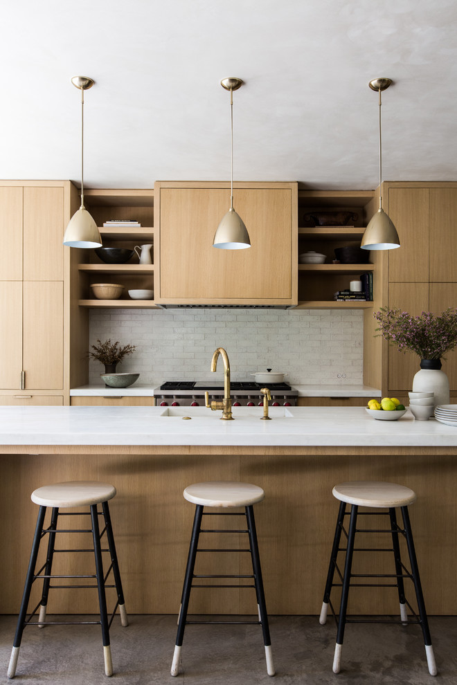 Foto på ett mellanstort funkis u-kök, med släta luckor, skåp i ljust trä, marmorbänkskiva, vitt stänkskydd, integrerade vitvaror, cementgolv och en köksö