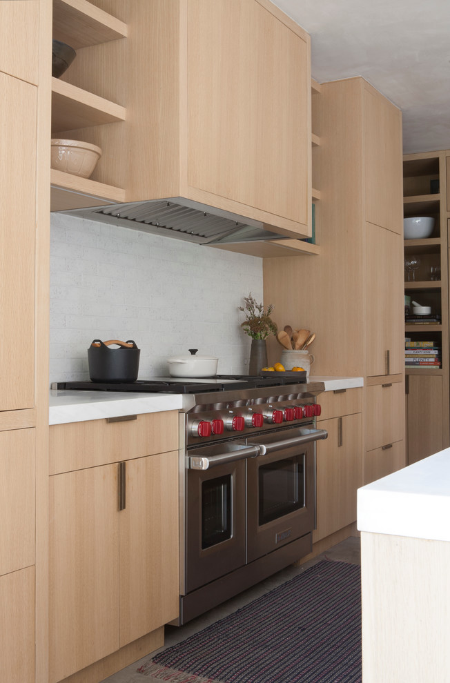 На фото: кухня-гостиная в стиле модернизм с плоскими фасадами, светлыми деревянными фасадами, мраморной столешницей, белым фартуком и бетонным полом