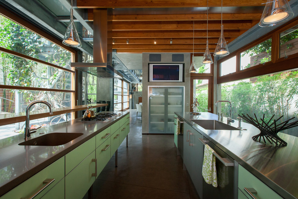 Пример оригинального дизайна: параллельная кухня в стиле лофт с монолитной мойкой, плоскими фасадами, зелеными фасадами, столешницей из нержавеющей стали, техникой из нержавеющей стали, бетонным полом, островом и серым полом