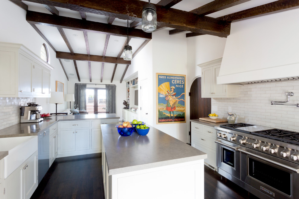 Photo of a mediterranean open plan kitchen in Los Angeles with a belfast sink, shaker cabinets, beige cabinets, white splashback, stainless steel appliances, dark hardwood flooring and an island.