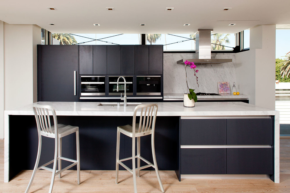 Inspiration for a contemporary galley light wood floor kitchen remodel in Los Angeles with an undermount sink, flat-panel cabinets, black cabinets, gray backsplash, paneled appliances and an island