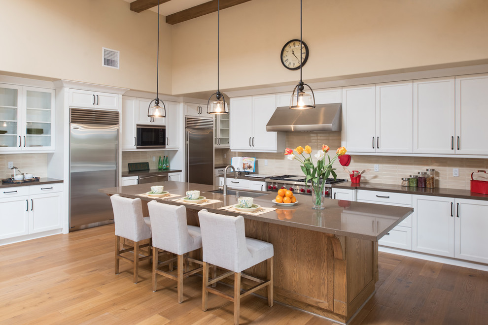 Mediterrane Küche in L-Form mit Unterbauwaschbecken, Schrankfronten im Shaker-Stil, weißen Schränken, Küchenrückwand in Beige, dunklem Holzboden, Kücheninsel, braunem Boden und brauner Arbeitsplatte in San Diego