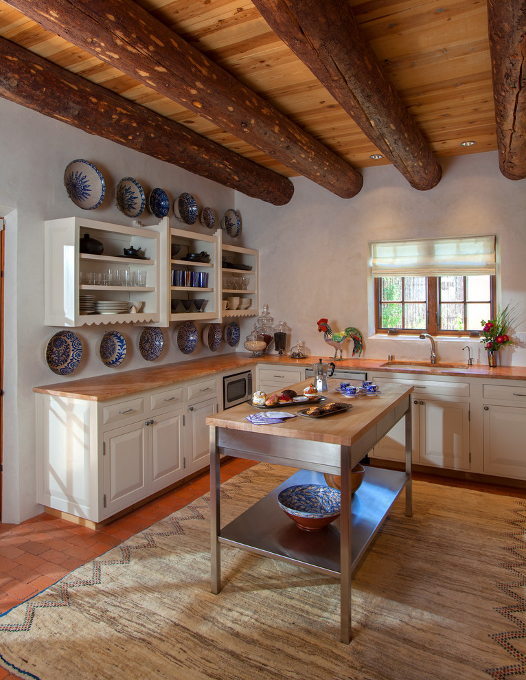 Пример оригинального дизайна: кухня в стиле фьюжн с обеденным столом, накладной мойкой, плоскими фасадами, белыми фасадами, деревянной столешницей, техникой из нержавеющей стали, кирпичным полом и островом