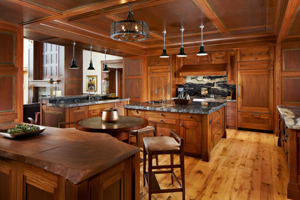 Foto på ett stort rustikt kök, med en undermonterad diskho, luckor med infälld panel, skåp i mellenmörkt trä, flerfärgad stänkskydd, integrerade vitvaror, mellanmörkt trägolv, flera köksöar, granitbänkskiva, stänkskydd i sten och beiget golv