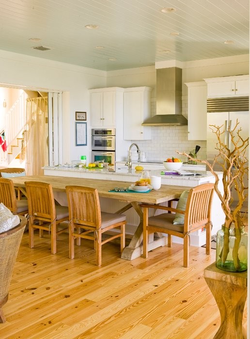 Maritim inredning av ett stort kök, med en köksö, skåp i shakerstil, vita skåp, marmorbänkskiva, vitt stänkskydd, stänkskydd i tunnelbanekakel, rostfria vitvaror och mellanmörkt trägolv