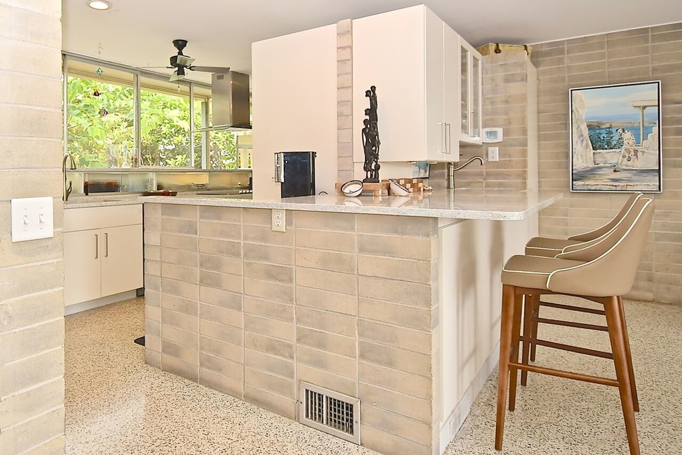 Example of a large 1950s galley terrazzo floor and white floor open concept kitchen design in Other with an integrated sink, flat-panel cabinets, white cabinets, quartz countertops, gray backsplash, stainless steel appliances, an island and white countertops