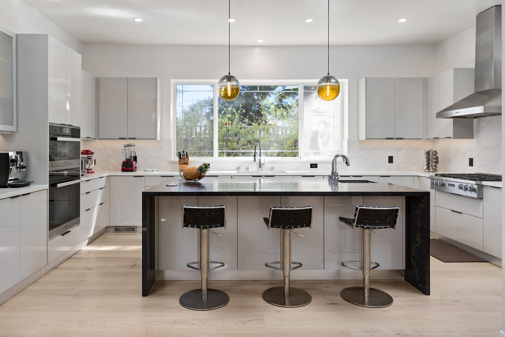 Moderne Küche in U-Form mit Unterbauwaschbecken, flächenbündigen Schrankfronten, grauen Schränken, Küchenrückwand in Weiß, Küchengeräten aus Edelstahl, hellem Holzboden, Kücheninsel, beigem Boden und weißer Arbeitsplatte in Sonstige