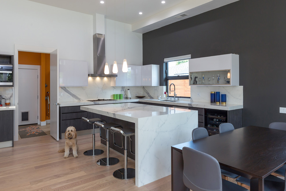 This is an example of a medium sized contemporary l-shaped kitchen/diner in San Francisco with a double-bowl sink, flat-panel cabinets, black cabinets, composite countertops, white splashback, marble splashback, stainless steel appliances, light hardwood flooring, an island, beige floors and white worktops.