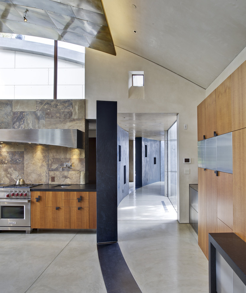 Foto på ett stort funkis kök, med rostfria vitvaror, släta luckor, skåp i mellenmörkt trä, brunt stänkskydd, en undermonterad diskho, bänkskiva i täljsten, stänkskydd i skiffer, betonggolv och en köksö