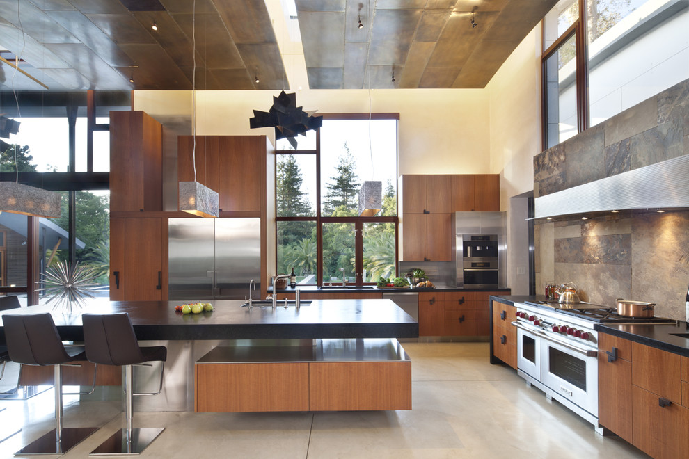 This is an example of a large contemporary l-shaped open plan kitchen in San Francisco with stainless steel appliances, flat-panel cabinets, medium wood cabinets, soapstone worktops, brown splashback, a submerged sink, slate splashback, concrete flooring and an island.