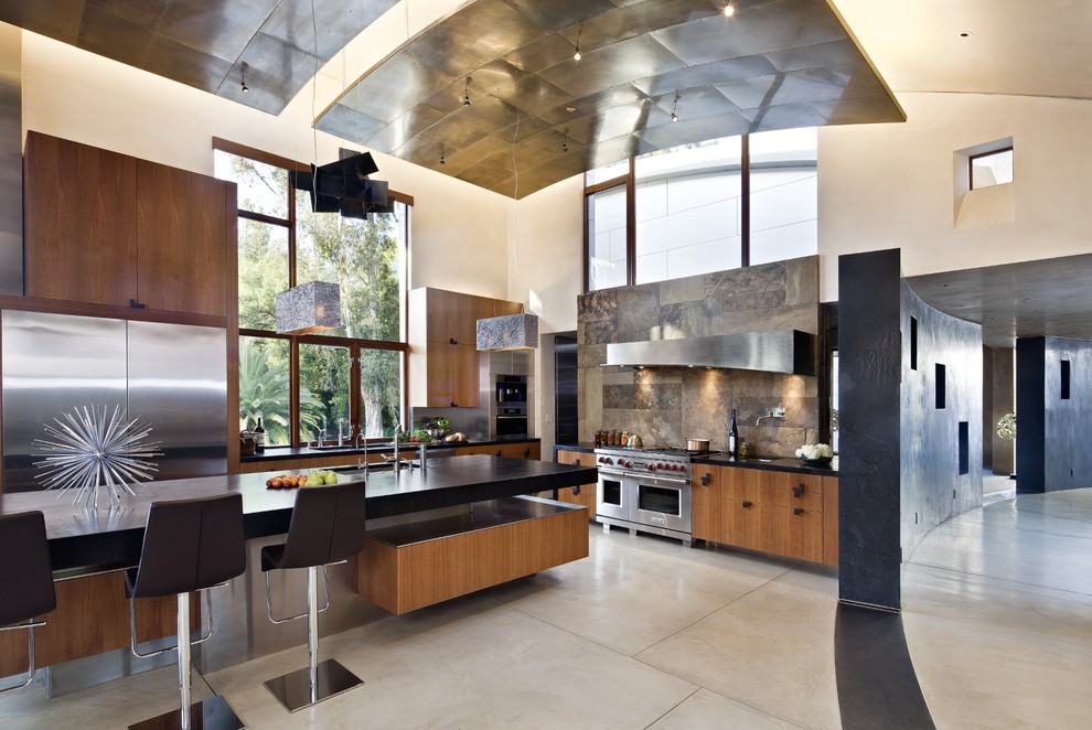 Large trendy l-shaped concrete floor and gray floor open concept kitchen photo in San Francisco with flat-panel cabinets, medium tone wood cabinets, soapstone countertops, brown backsplash, stainless steel appliances, slate backsplash, an undermount sink and an island