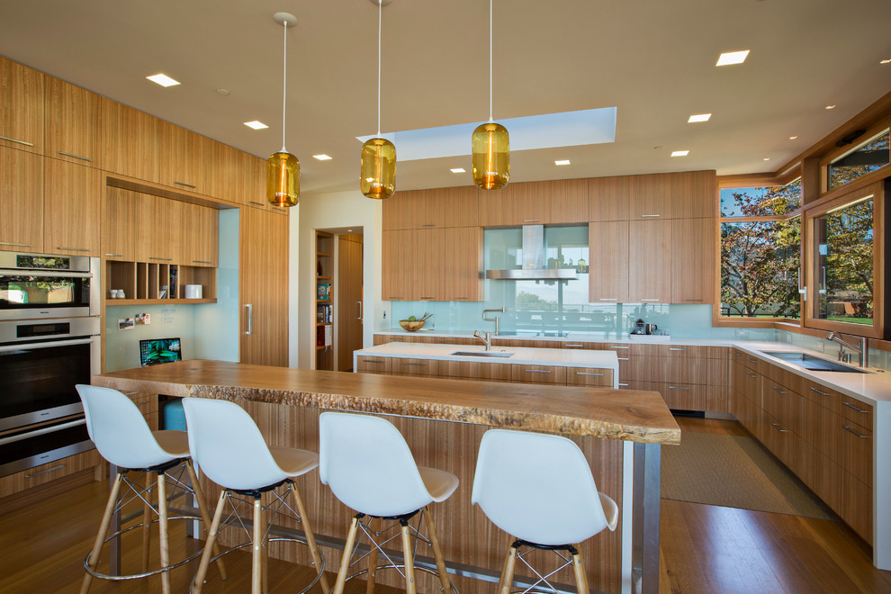 Photo of a contemporary u-shaped kitchen in San Francisco with a submerged sink, flat-panel cabinets, medium wood cabinets, glass sheet splashback, stainless steel appliances, medium hardwood flooring and multiple islands.