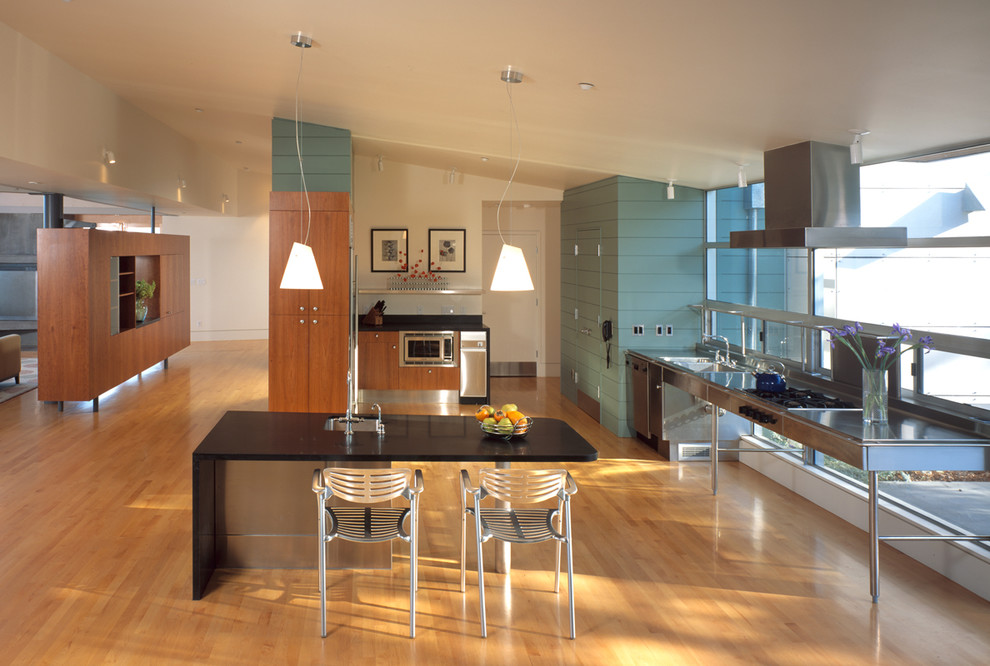 Modern inredning av ett kök med öppen planlösning, med rostfria vitvaror och bänkskiva i rostfritt stål