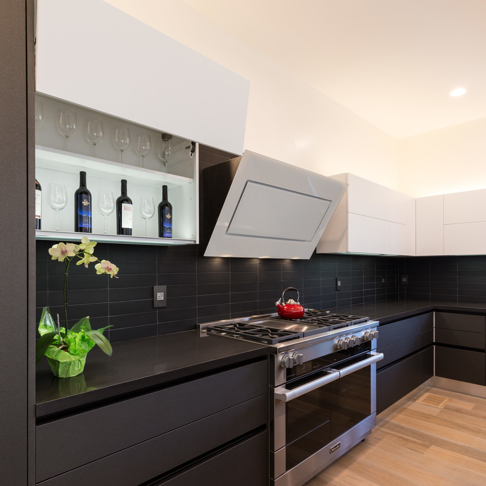 Example of a large minimalist u-shaped medium tone wood floor and brown floor open concept kitchen design in San Francisco with an undermount sink, flat-panel cabinets, black cabinets, quartz countertops, black backsplash, ceramic backsplash, stainless steel appliances, an island and black countertops