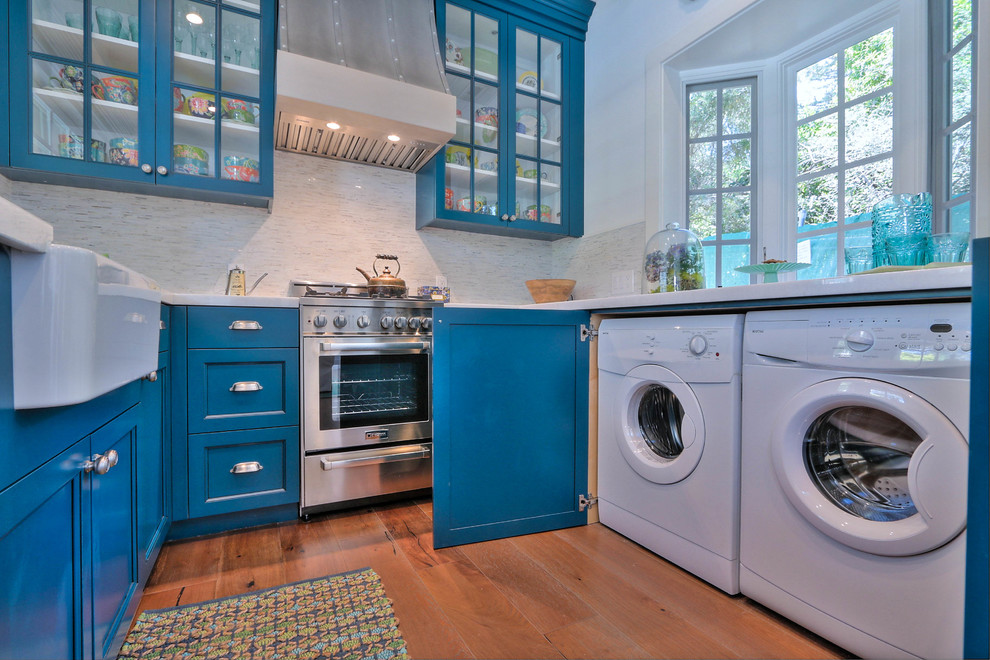Cette image montre une petite cuisine marine en U avec un évier de ferme, un placard à porte vitrée, des portes de placard bleues et un sol en bois brun.