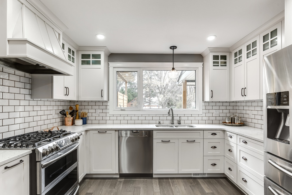 Example of a classic u-shaped medium tone wood floor and brown floor kitchen design in Other with an undermount sink, shaker cabinets, white cabinets, white backsplash, subway tile backsplash, stainless steel appliances and no island