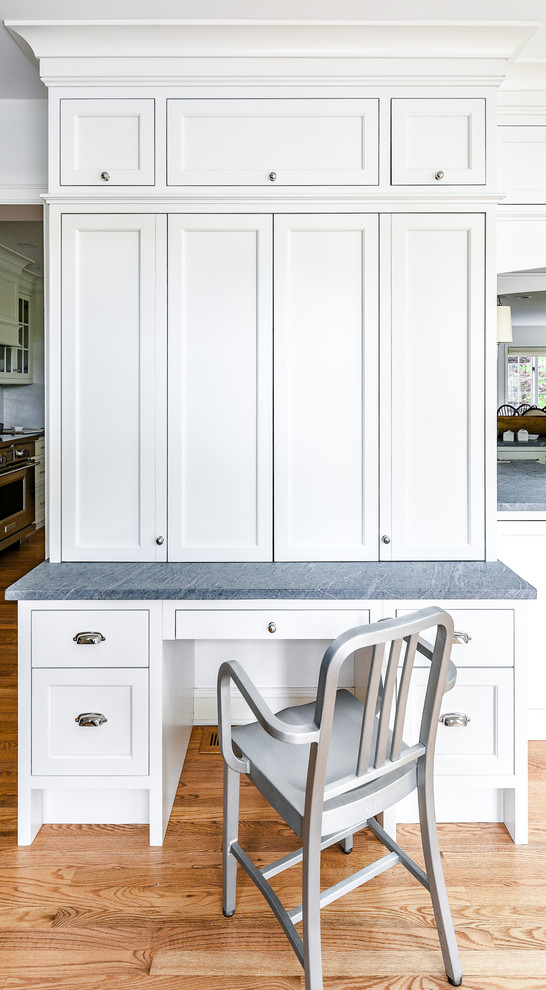 Large transitional l-shaped light wood floor eat-in kitchen photo in Philadelphia with a farmhouse sink, flat-panel cabinets, white cabinets, soapstone countertops, white backsplash, ceramic backsplash, paneled appliances, an island and gray countertops