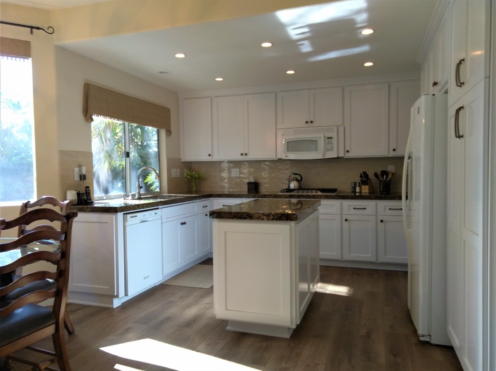 Photo of a medium sized traditional u-shaped kitchen/diner in Los Angeles with a double-bowl sink, shaker cabinets, white cabinets, granite worktops, yellow splashback, ceramic splashback, white appliances, an island, brown floors and brown worktops.