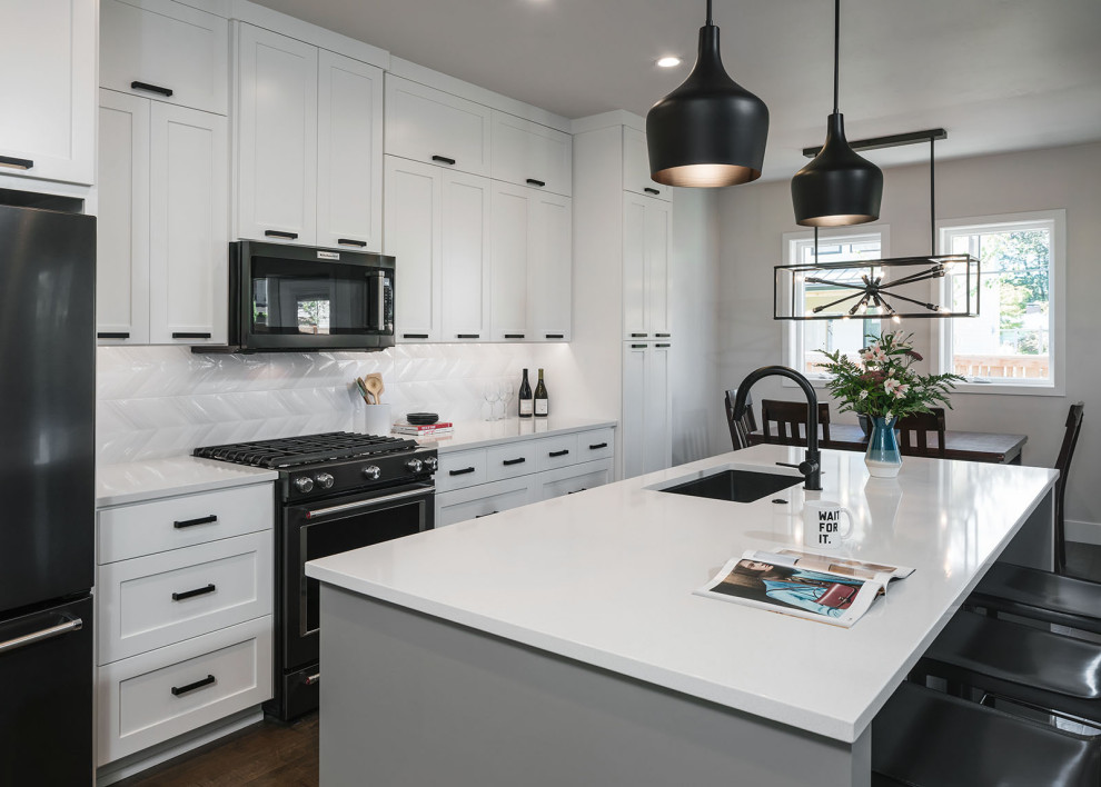Example of a mid-sized transitional single-wall dark wood floor and brown floor eat-in kitchen design in Other with an undermount sink, shaker cabinets, white cabinets, quartz countertops, white backsplash, ceramic backsplash, black appliances, an island and white countertops