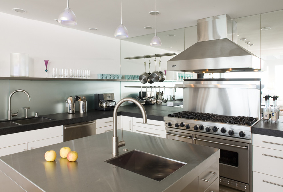 Bild på ett stort funkis kök, med en undermonterad diskho, släta luckor, vita skåp, granitbänkskiva, grönt stänkskydd, glaspanel som stänkskydd, rostfria vitvaror, ljust trägolv och en köksö