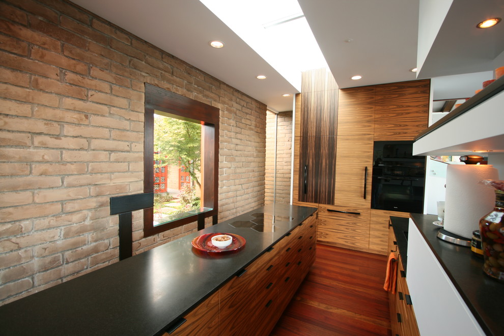 Immagine di una grande cucina moderna con lavello sottopiano, ante lisce, ante in legno scuro, top in granito, paraspruzzi nero, paraspruzzi in lastra di pietra, elettrodomestici da incasso e parquet scuro