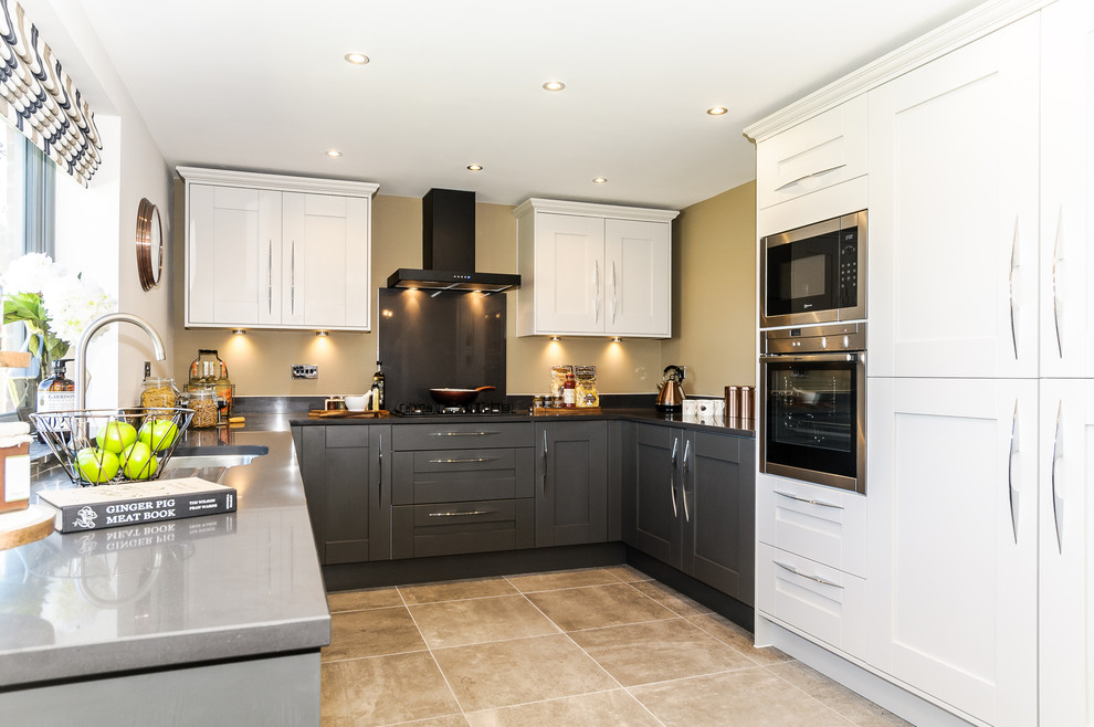 This is an example of a medium sized classic u-shaped kitchen/diner in Dorset with a submerged sink, shaker cabinets, stainless steel appliances, no island, grey cabinets, composite countertops, black splashback, stone slab splashback and ceramic flooring.