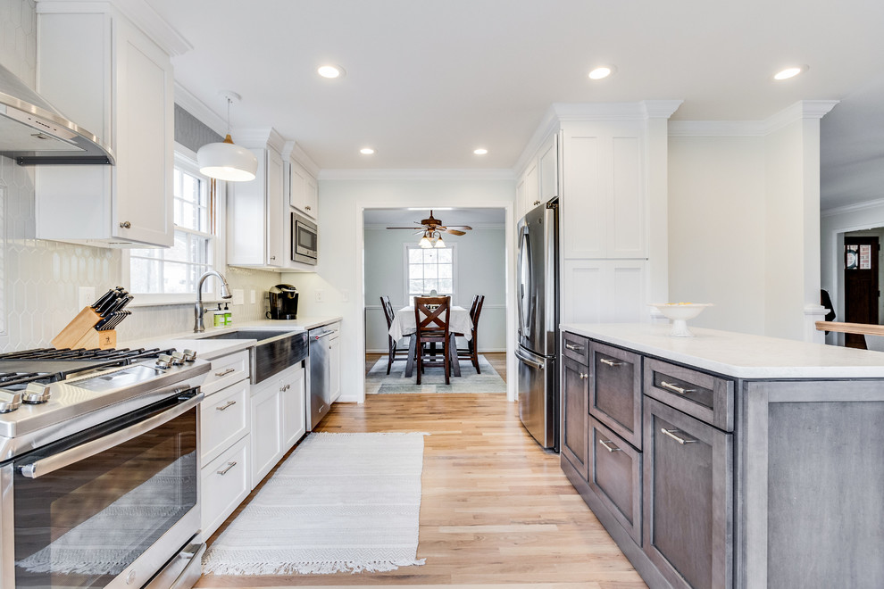 Enclosed kitchen - mid-sized country galley light wood floor enclosed kitchen idea in Birmingham with a farmhouse sink, shaker cabinets, white cabinets, quartz countertops, gray backsplash, ceramic backsplash, stainless steel appliances, an island and gray countertops