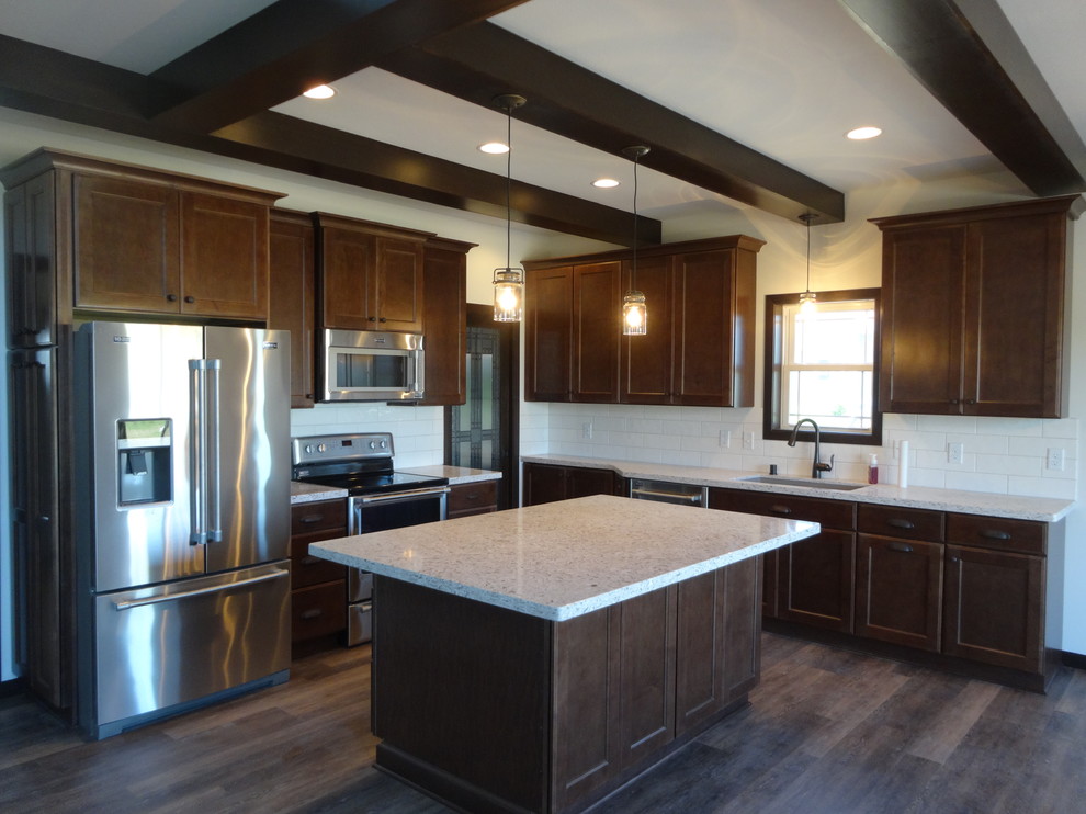 Inspiration for a large traditional l-shaped open plan kitchen in Milwaukee with a submerged sink, recessed-panel cabinets, dark wood cabinets, engineered stone countertops, white splashback, cement tile splashback, stainless steel appliances, vinyl flooring, an island and brown floors.