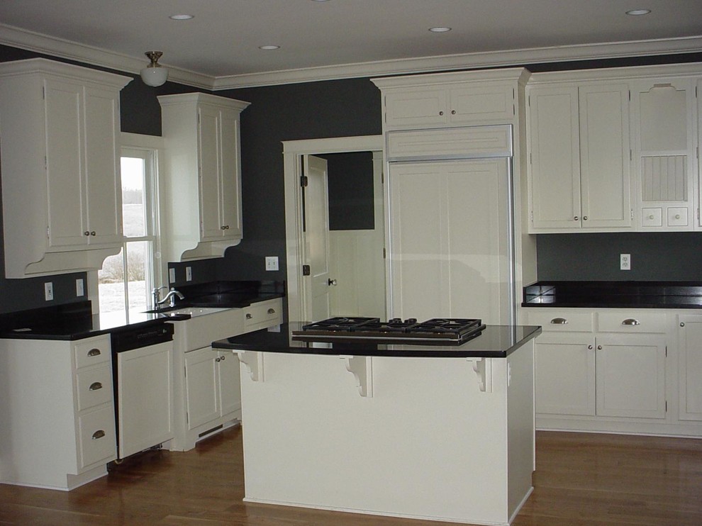 This is an example of a farmhouse l-shaped kitchen/diner in DC Metro with a belfast sink, shaker cabinets, white cabinets, granite worktops and integrated appliances.