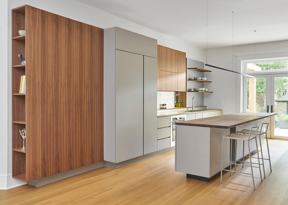 Cette image montre une cuisine linéaire et encastrable minimaliste avec un placard à porte plane, des portes de placard grises, un plan de travail en bois, îlot, un sol marron, un sol en bois brun et un plan de travail marron.