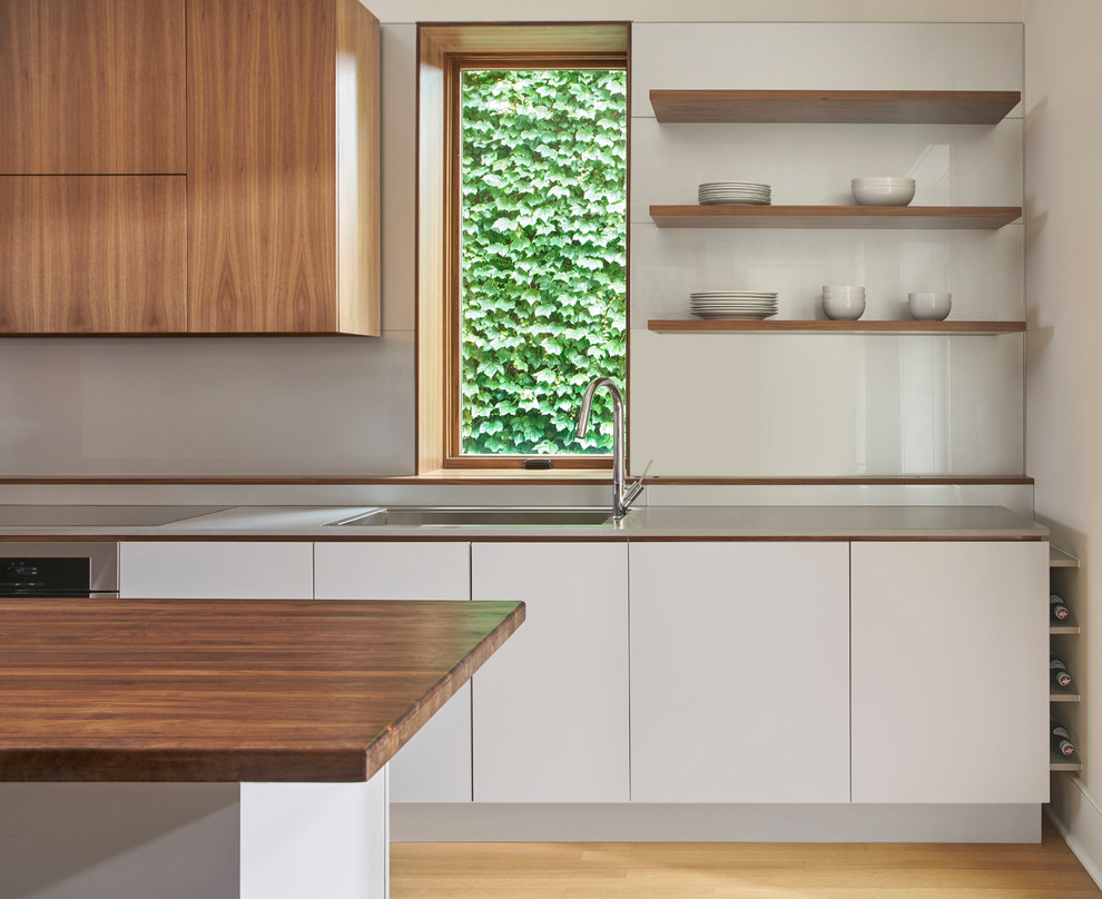 Inredning av ett modernt linjärt kök, med släta luckor, grå skåp, träbänkskiva, glaspanel som stänkskydd, integrerade vitvaror, ljust trägolv, en köksö och brunt golv