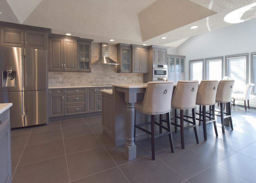 Example of a large transitional l-shaped open concept kitchen design in New York with raised-panel cabinets, gray cabinets, quartz countertops, beige backsplash, stone tile backsplash, stainless steel appliances and an island